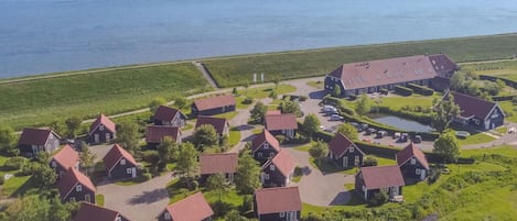 An aerial view of a coastal village with houses, a large barn, and a small lake.