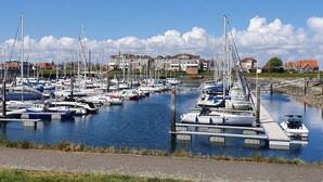 A marina with numerous boats docked, a clear sky, and residential buildings in the background. - Beautiful apartment in villa for 5 people with WIFI, TV, terrace and panoramic view (Wemeldinge)