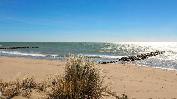 A beach with sand, grass, and a rocky breakwater. - Stunning home in Arles (Arles)