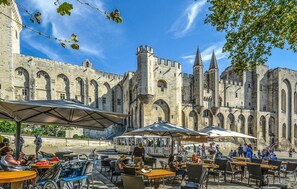 A historic building with arched windows and towers, outdoor seating with umbrellas, and a tram in the background. - Stunning home in Arles (Arles)