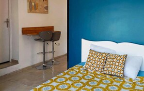 A room with a bed, a blue headboard, a patterned bedspread, two bar stools, and a wooden shelf. - Stunning home in Arles (Arles)