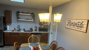 A kitchen with wooden cabinets, a dining table with chairs, a chandelier, and a wall sign. - Comfortable 3BR Home w/ POOL! Near Lackland AFB & Seaworld for BMT Families (San Antonio)
