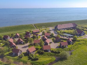 Luchtbeeld van een kustdorp met huizen, een grote schuur en een wateroppervlak.