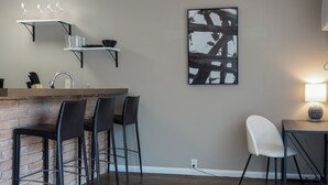 Eine moderne Küche mit Ziegelrückwand, schwarzen Barhocker, einem weißen Stuhl und einem an der Wand hängenden abstrakten Gemälde.