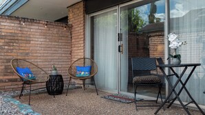 Eine Terrasse mit einer Backsteinmauer, zwei Korbstühlen mit bunten Kissen, einem kleinen runden Tisch und einem Topfpflanzen.