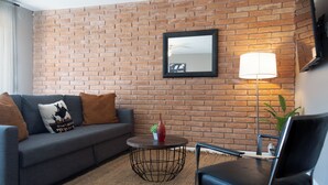 Ein Wohnzimmer mit Backsteinwand, einer Couch mit Zierkissen, einem runden Couchtisch, einem Sessel und einer Stehlampe.