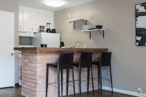 A kitchen with a brick island, bar stools, white cabinets, a white refrigerator, and a black coffee machine.