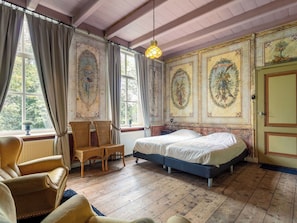 Una habitación con una cama, dos sillas de mimbre, una ventana con cortinas y un muro con paneles decorativos.