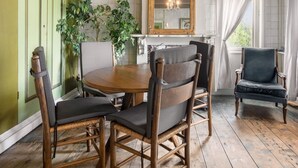 Un coin repas comprenant une table ronde en bois, quatre chaises, un miroir et une fenêtre avec des rideaux.
