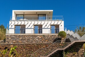 A modern two-story house with a stone facade, large windows, and a balcony.