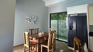 Een eetruimte met een houten tafel en stoelen, een plafondventilator, een koelkast en een schuifdeur naar een tuin.