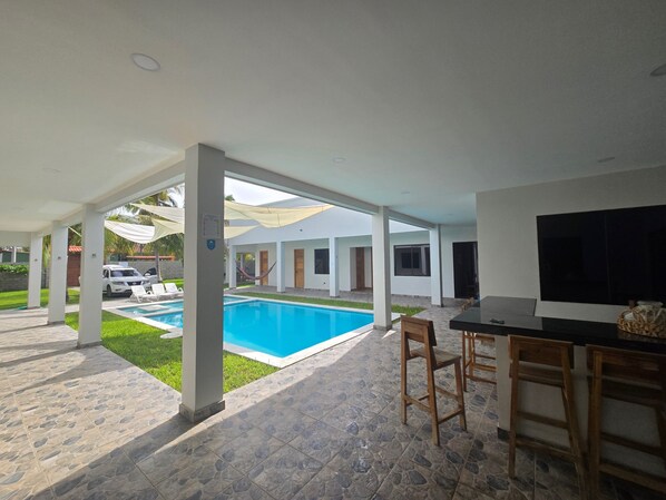 Un espacio al aire libre cubierto con una piscina, una mesa de comedor con sillas y un televisor.