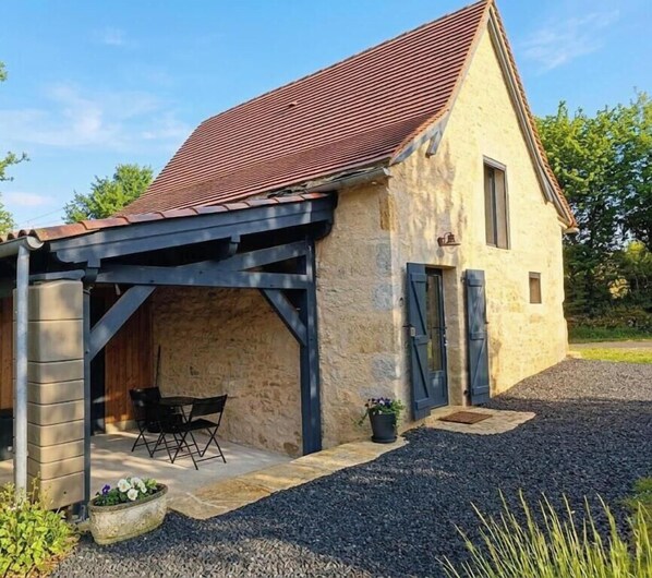 Ein rustikales Steinhaus mit überdachter Terrasse, einem kleinen Tisch und Stühlen.