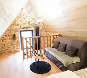 Ein gemütliches Schlafzimmer im Loft-Stil mit Steinwand, Holztreppe, einer Couch und einem kleinen Tisch mit Lampe.