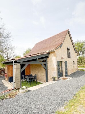 Ein eingeschossiges Haus mit geneigtem Dach, einer überdachten Terrasse mit Tisch und Stühlen sowie einer Auffahrt mit Kies.