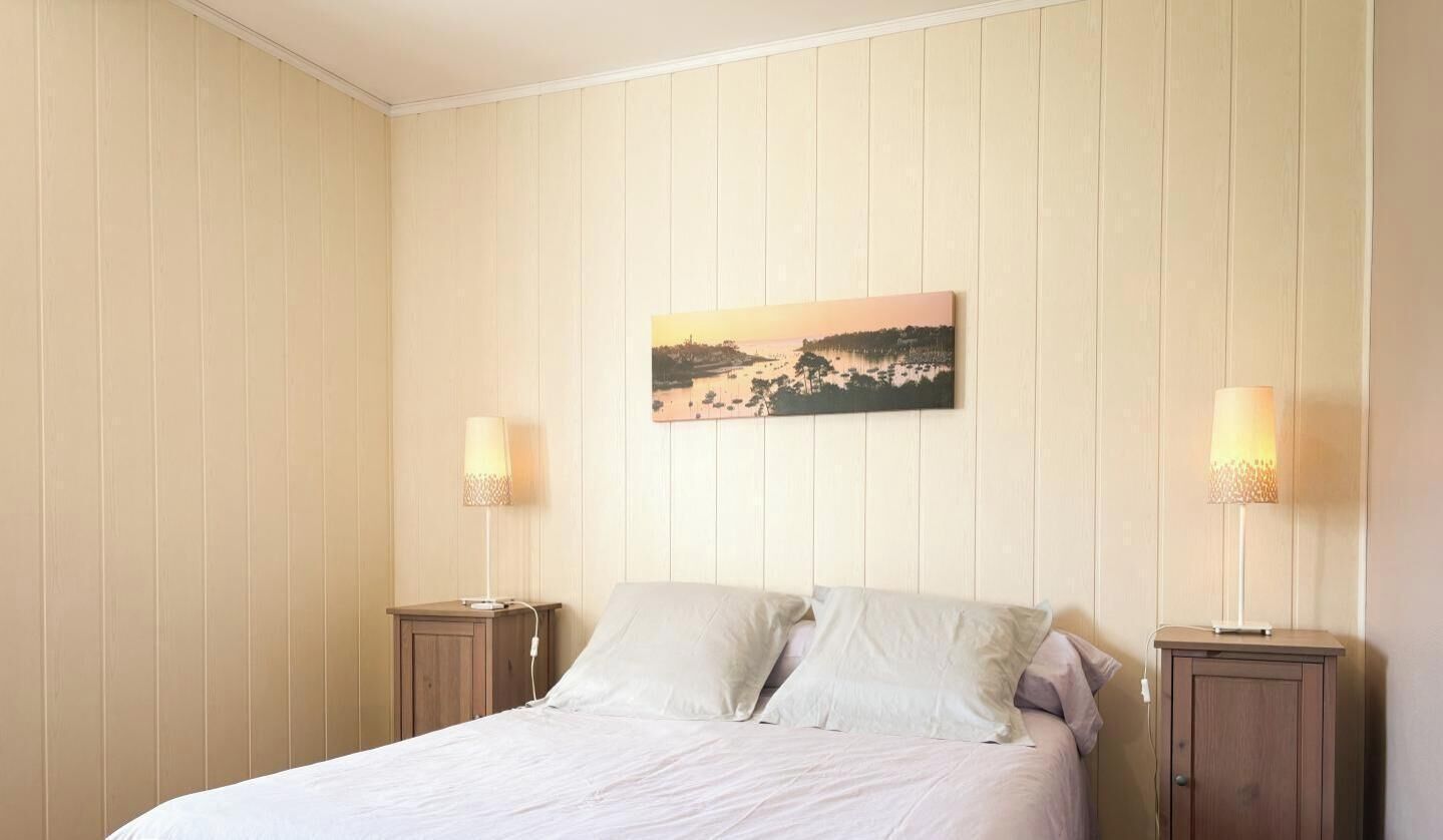 Une chambre à coucher comprenant un lit, deux tables de chevet, une petite table et un tableau accroché au mur.