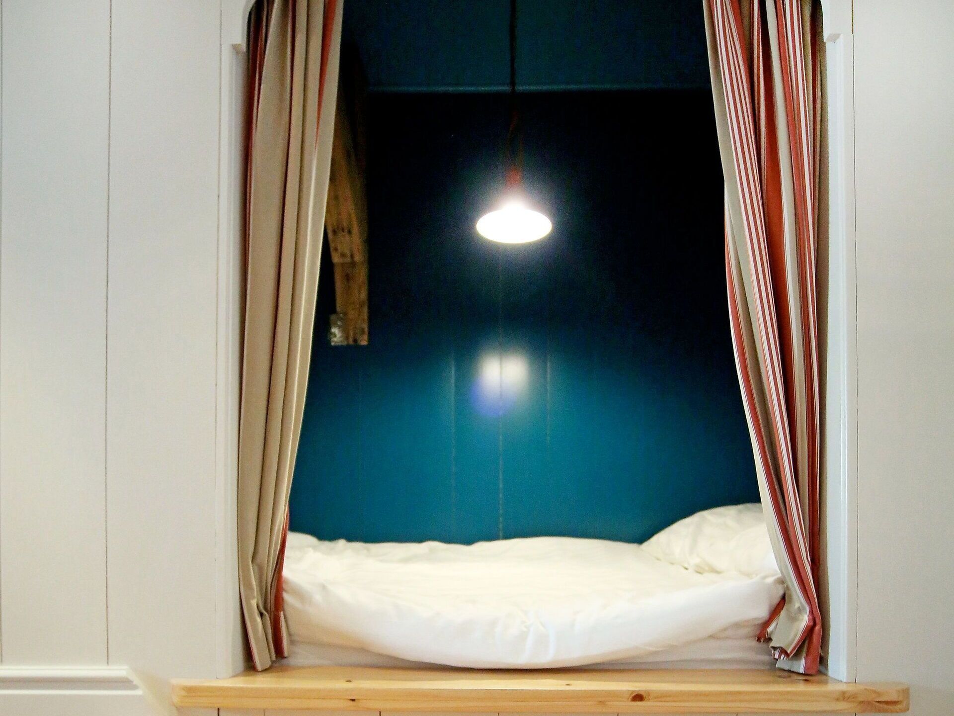Une pièce avec un lit, des rideaux, un luminaire suspendu et un mur bleu.