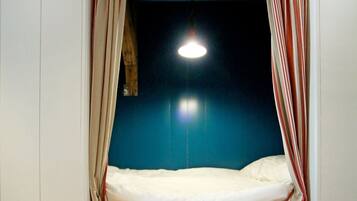 Une pièce avec un lit, des rideaux, un luminaire suspendu et un mur bleu.