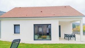 Ein modernes Haus mit einem Ziegeldach, einer großen Schiebeglastür und einer Terrasse mit Gartenmöbeln.