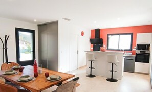 Une cuisine moderne dotée d’un îlot central, de tabourets de bar et d’un coin repas avec une table dressée pour quatre personnes.