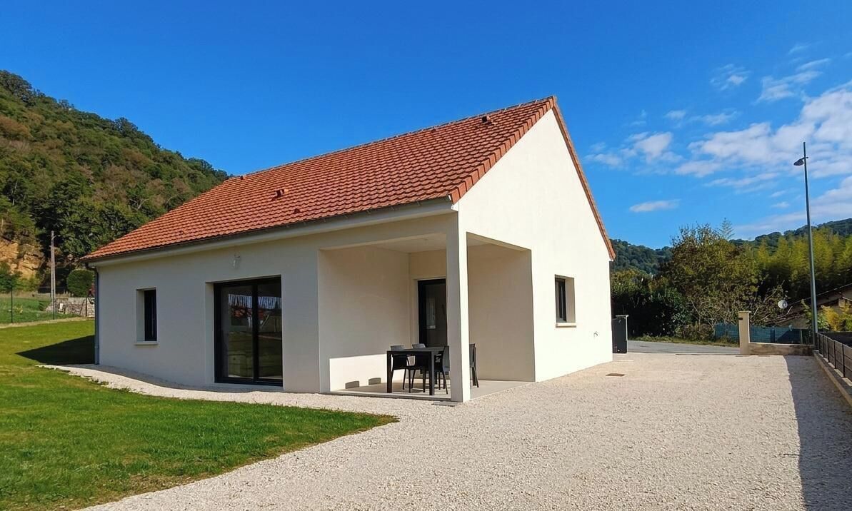 Un bâtiment d’un seul étage, doté d’un toit recouvert de tuiles rouges, d’un patio abrité avec une table et des chaises, et d’une allée en gravier.