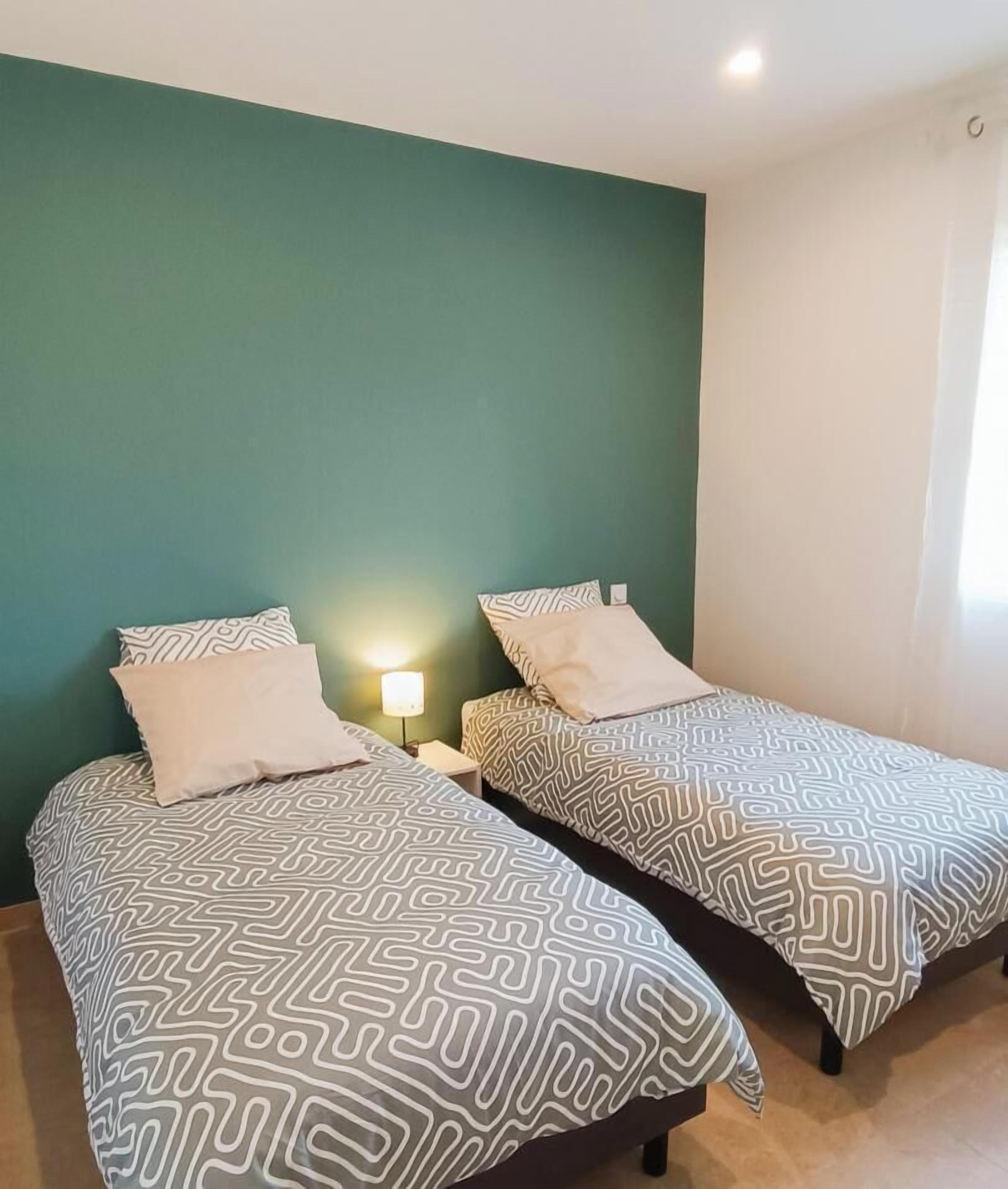 Deux lits simples avec une literie à motifs, une table de chevet avec une lampe et un mur vert.