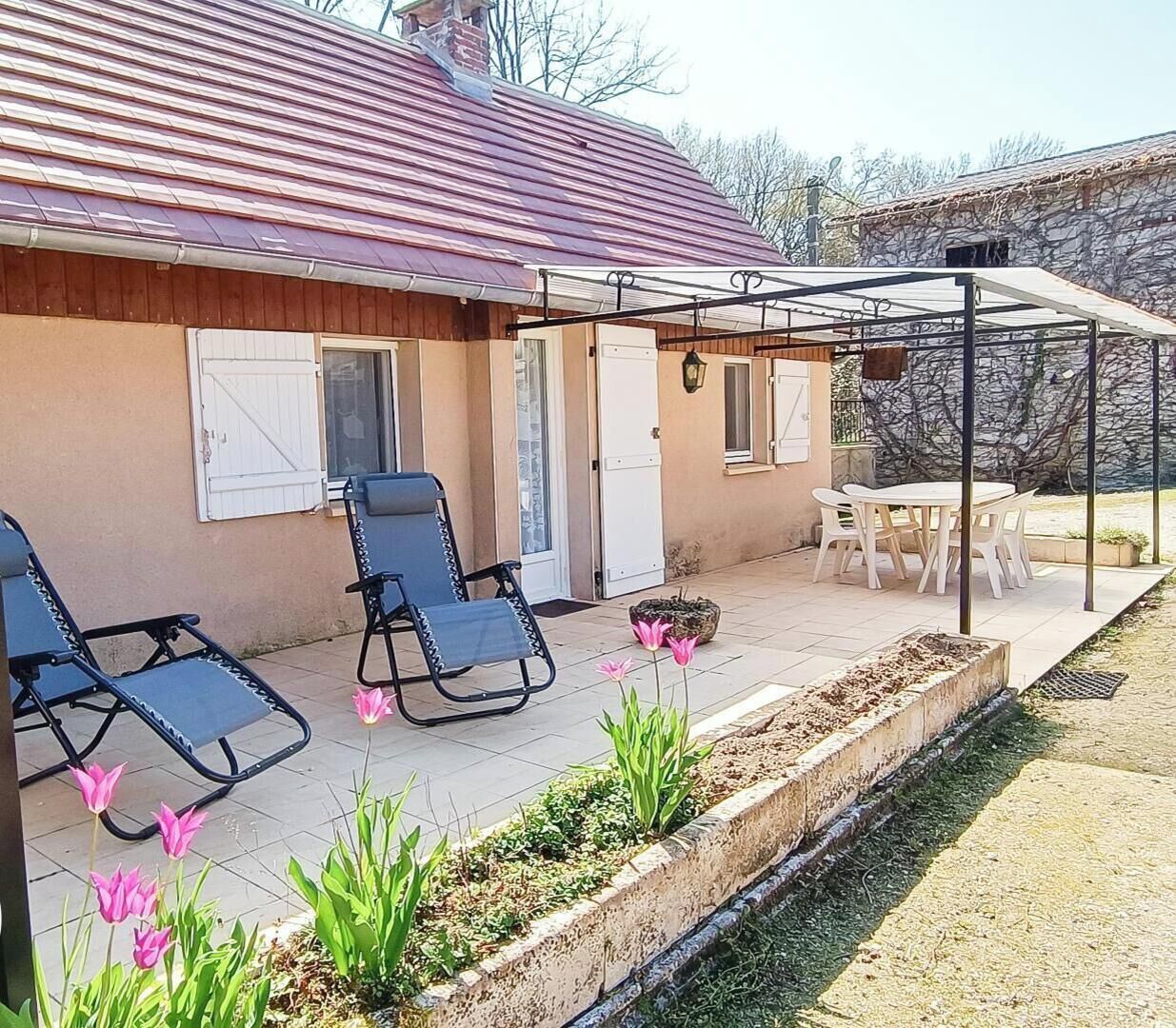 A house with a covered patio, two lounge chairs, a table, and a garden with tulips.