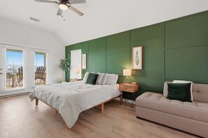 Ein Schlafzimmer mit Bett, Nachttisch, Sofa, Deckenventilator und Blick durch ein Fenster.
