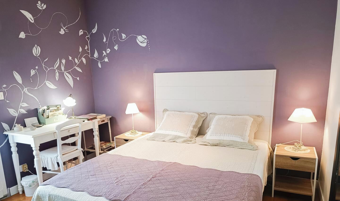A bedroom with a bed, two bedside tables, a desk with a chair, and a wall with a leaf pattern.