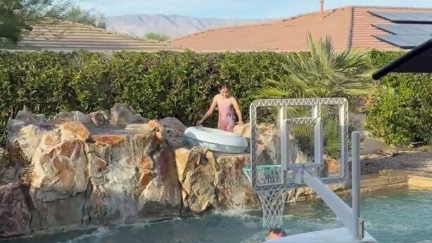 Piscina com aro de basquete, parede de escalada e céu claro.