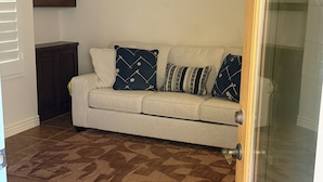 Uma sala de estar com um sofá bege, almofadas estampadas, um armário de madeira escura e um tapete com padrão marrom.