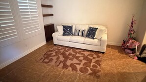 Sala de estar com sofá branco, tapete estampado e ventilador de teto.