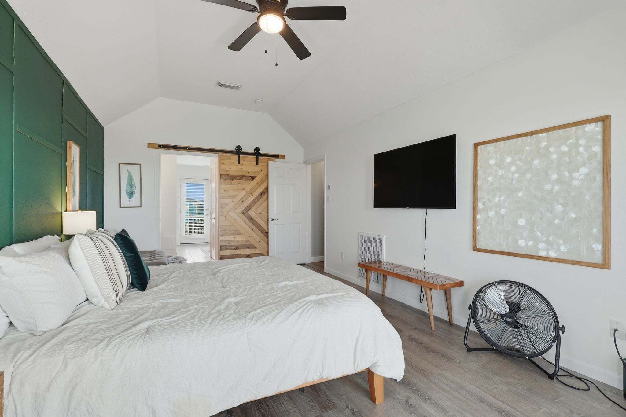 A bedroom with a bed, a ceiling fan, a TV, and a large abstract painting.