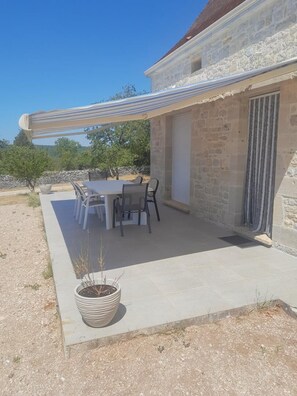 A stone building with a patio, outdoor table, chairs, and a potted plant. - Gîtes de la Gariotte - QUISSAC-EN-QUERCY (QUISSAC-EN-QUERCY)