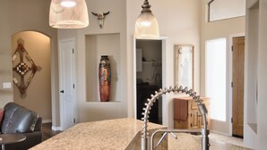 A kitchen with granite countertops, a stainless steel sink, pendant lights, and a decorative wall piece.