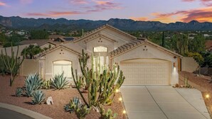 A residential house with a garage, surrounded by desert plants and mountains in the background.