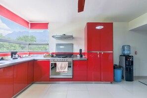 A kitchen with red cabinets, a gas stove, a water dispenser, and a view of mountains through the window. - ¡Departamento en Bosques del Valle! - 5 guests (San Pedro Garza García)