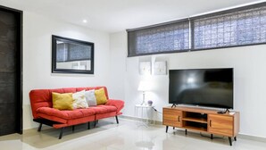 Un salón con un sofá rojo, un televisor sobre un mueble de madera, una ventana con persianas y un cuadro en la pared.