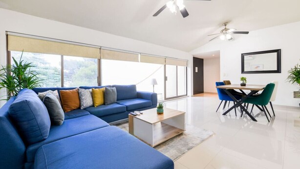 Una sala de estar moderna con un sofá seccional azul, una mesa de centro y un comedor con una mesa y sillas.