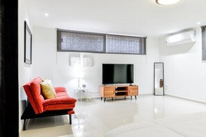 A modern living room with a flat-screen TV, a red sofa, a small side table, and a wooden cabinet. - ¡Departamento en Bosques del Valle! - 5 guests (San Pedro Garza García)