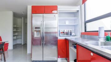 A modern kitchen with a stainless steel refrigerator, red cabinets, a microwave, and a sink with a window above.