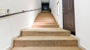 Una escalera con alfombra, barandilla, una puerta oscura y un interruptor de luz en la pared.