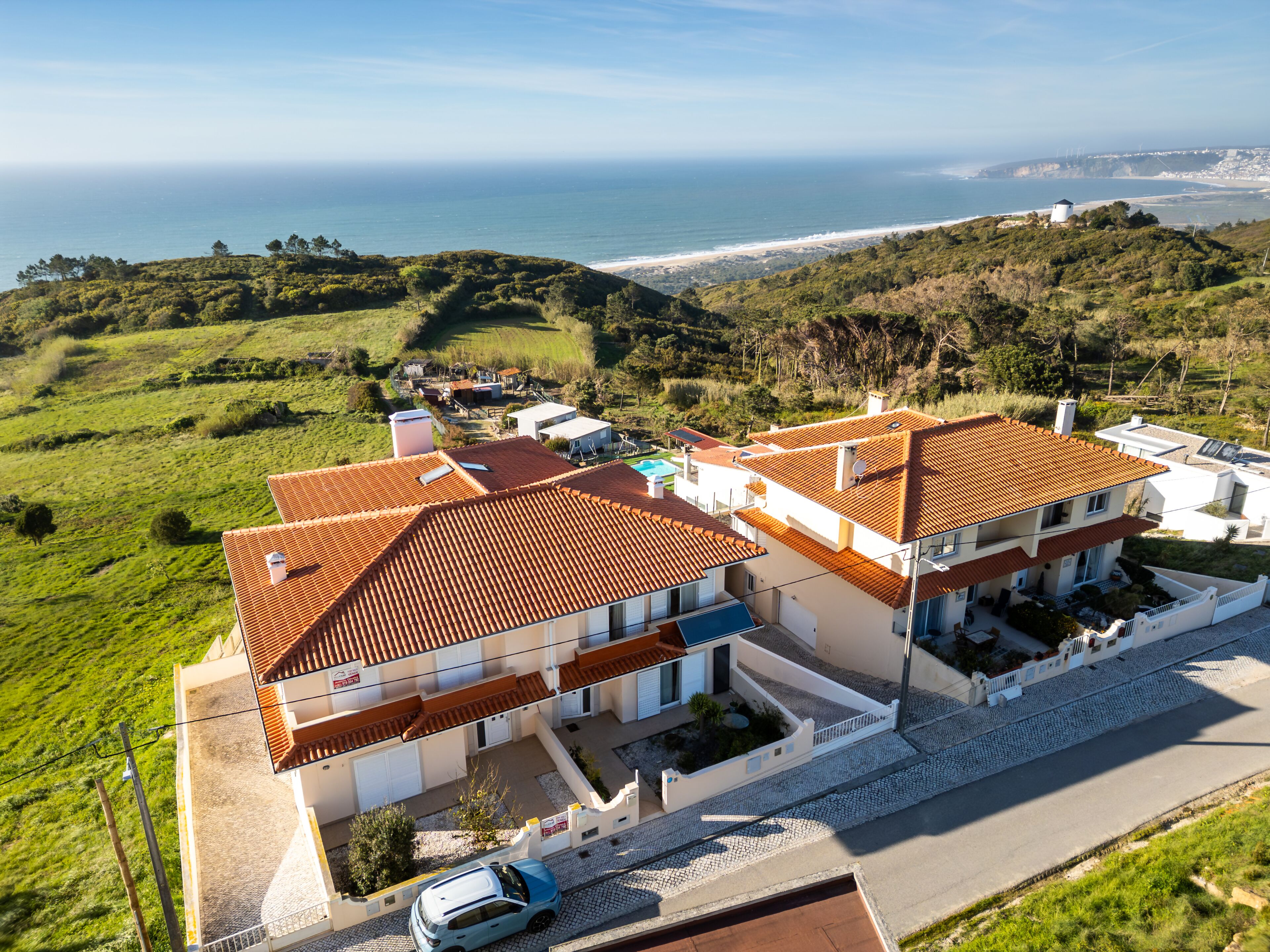 A two-story building with a red-tiled roof, a swimming pool, and a view of the ocean.