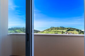 A view from a window with a clear sky, a green hill, and a distant building.
