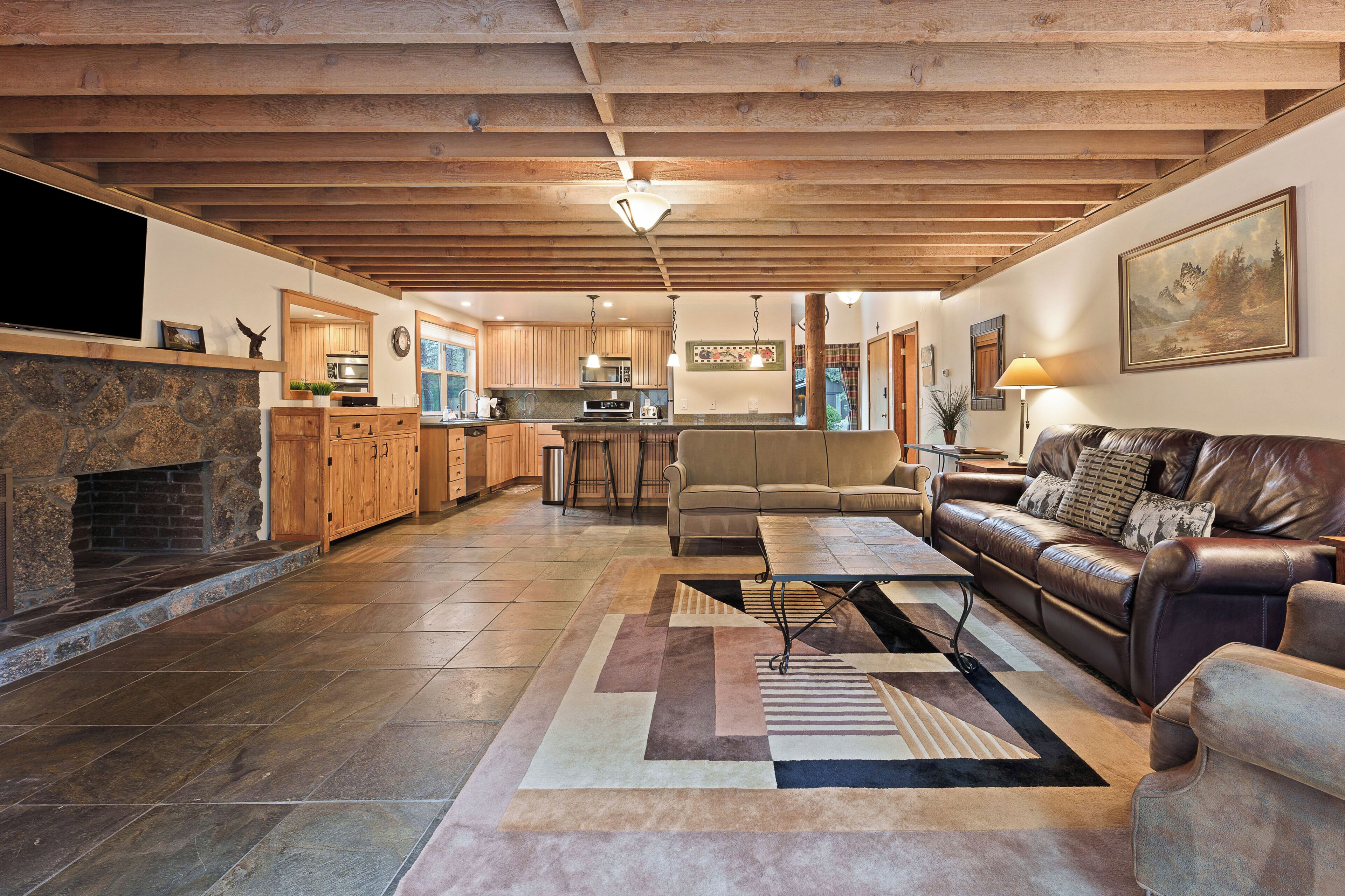 A spacious living room with a fireplace, a leather sofa, and a kitchen in the background.