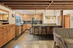Una cocina con armarios de madera, una isla central con taburetes, un refrigerador y un área de comedor con un sofá.