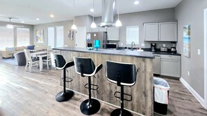 Una cocina moderna con una isla central, taburetes de bar, ventilador de techo y comedor con sofá y sillas.