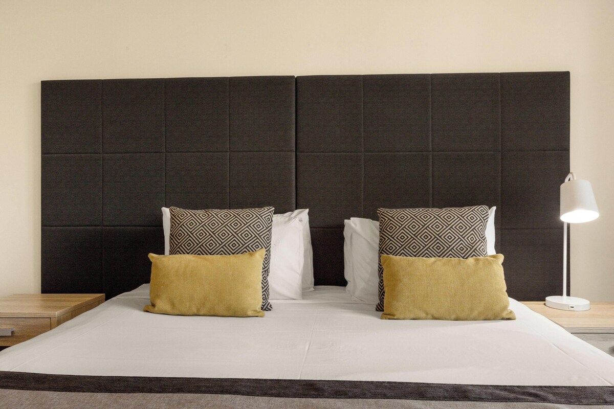 A bed with a dark headboard, two patterned pillows, and a bedside lamp.