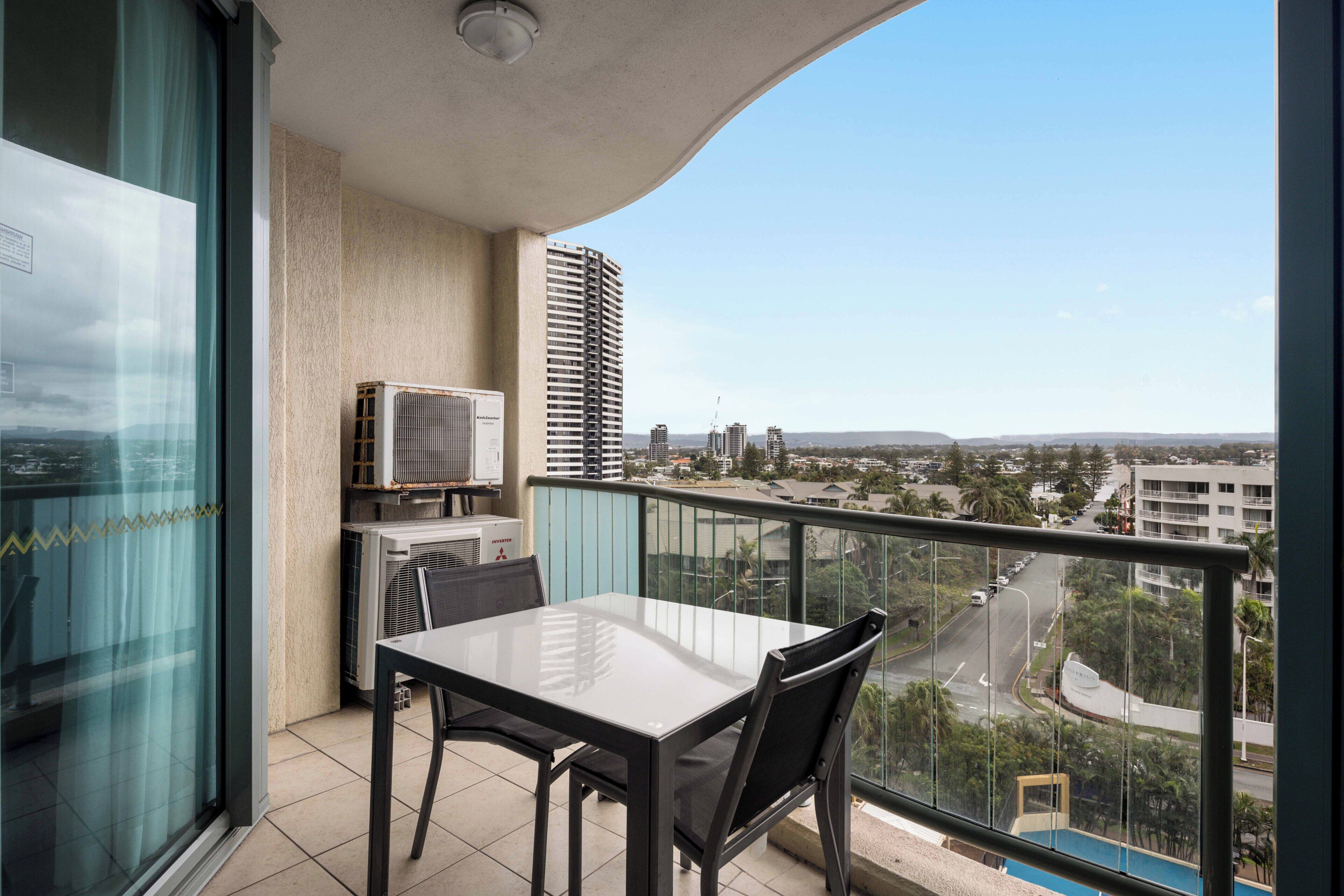 A balcony with a table and chairs, an air conditioning unit, and a view of the cityscape.