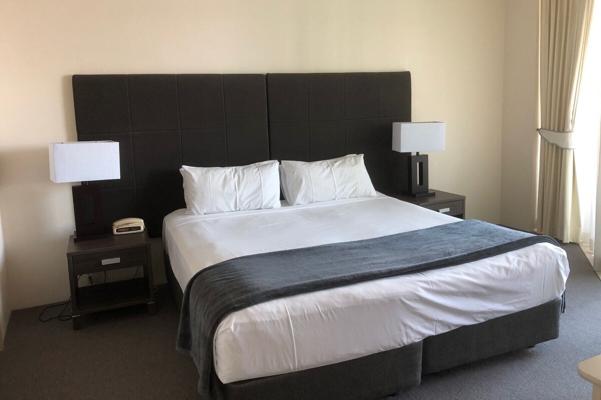 A hotel room with a large bed, two bedside tables, a lamp on each table, and a window with curtains.
